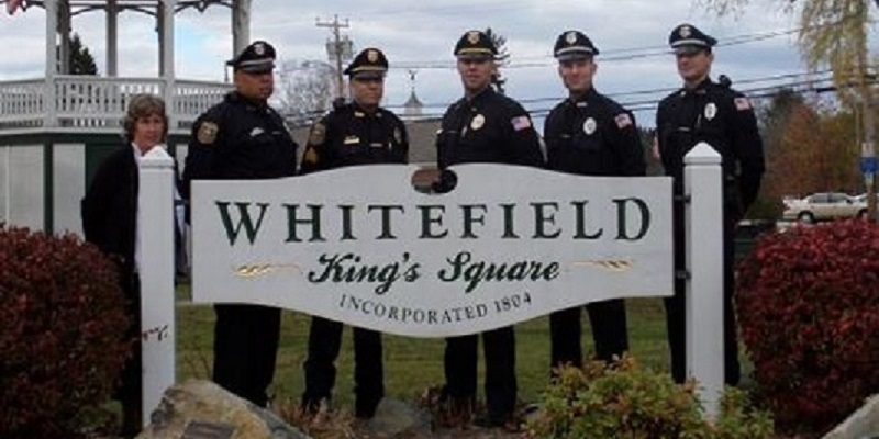 Police Officers standing Behind Whitefield Town SigS