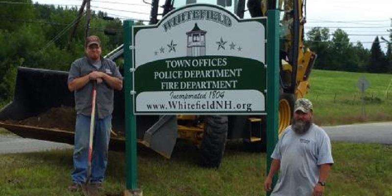 Two Construction Workers Standing Next to Whitefield Town Sign
